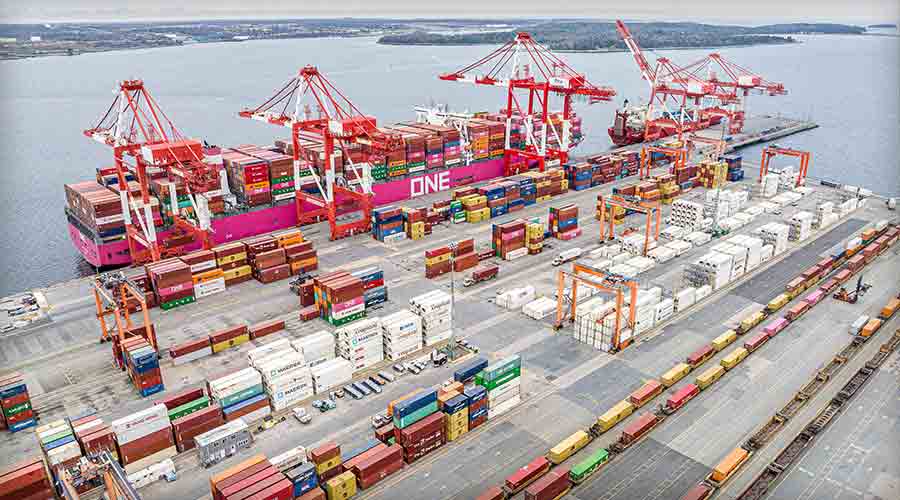 Aerial view of Fairview Cove container terminal at the Port of Halifax on Bedford Basin — an Ocean Network Express container ship worked by ship-to-shore gantry cranes, with reefer racks and an on-dock CN rail yard of intermodal railcars in the foreground