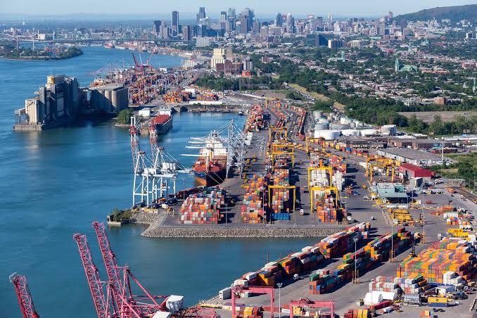 Aerial view of the Port of Montreal container terminals along the St. Lawrence River with the Montreal skyline in the background