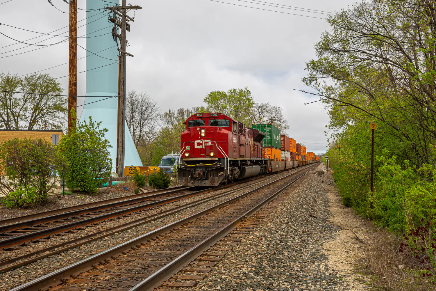 A CP (Canadian Pacific) locomotive leading a double-stacked intermodal container train past a trackside water tower